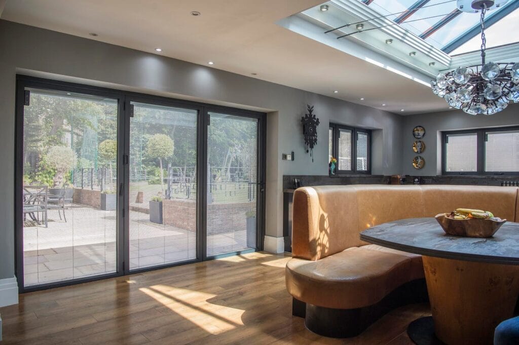 Interior view of a garden room with anthracite sliding patio doors fitted with integral blinds, overlooking a landscaped garden