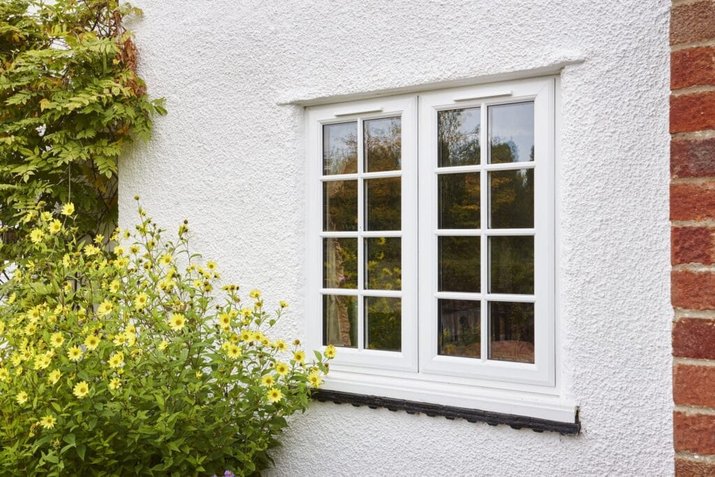 georgian style uPVC window on a white-walled house, next to a yellow flower bush.
