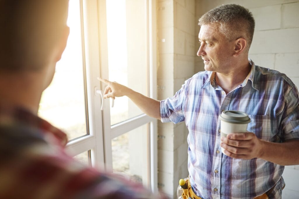 Installer pointing out features of a newly fitted white uPVC window to a colleague during a home renovation.