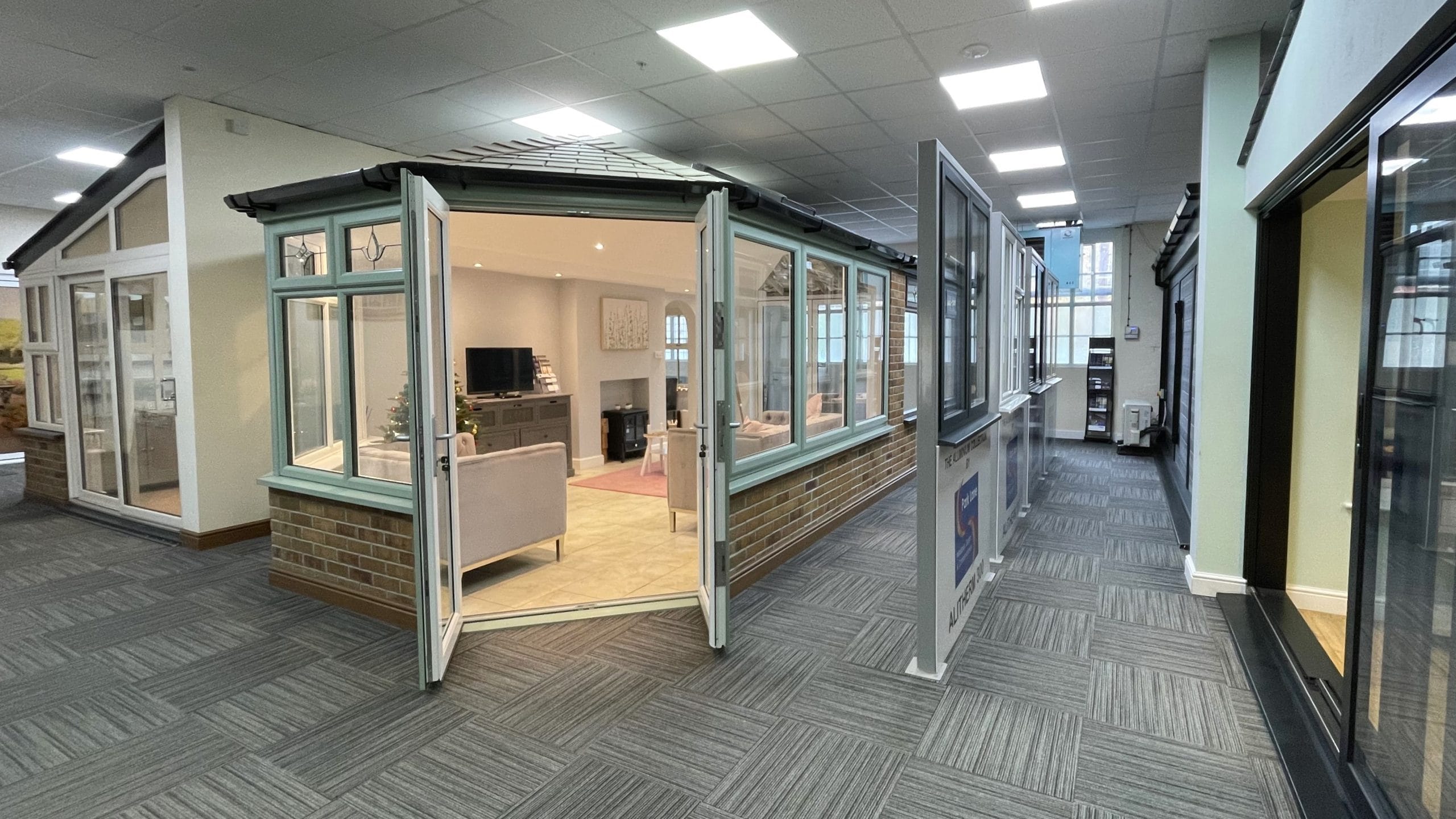 Park Lane Windows showroom interior featuring a full-size conservatory display with open sage green bi-fold doors