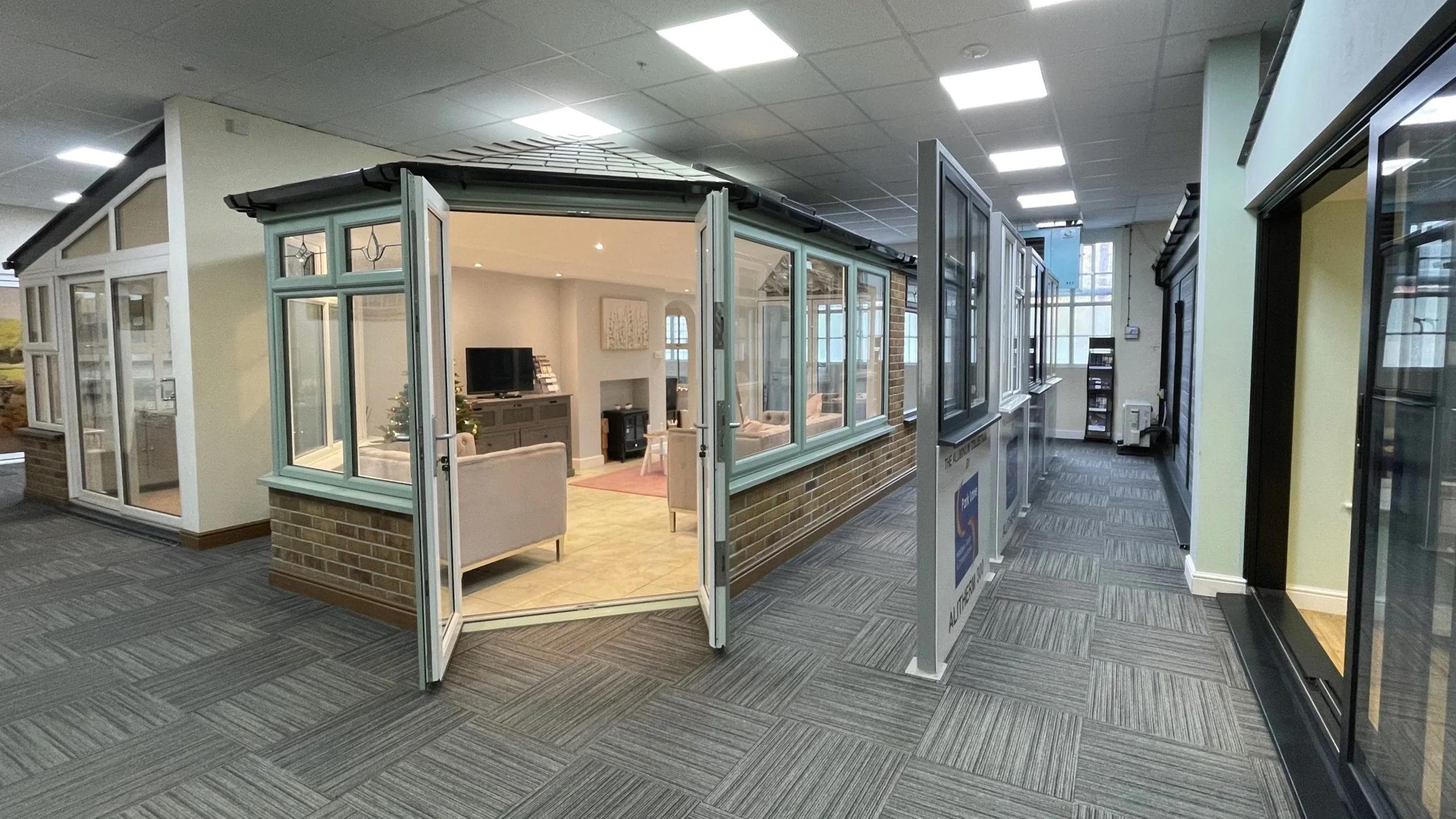 Park Lane Windows showroom interior featuring a full-size conservatory display with open sage green bi-fold doors