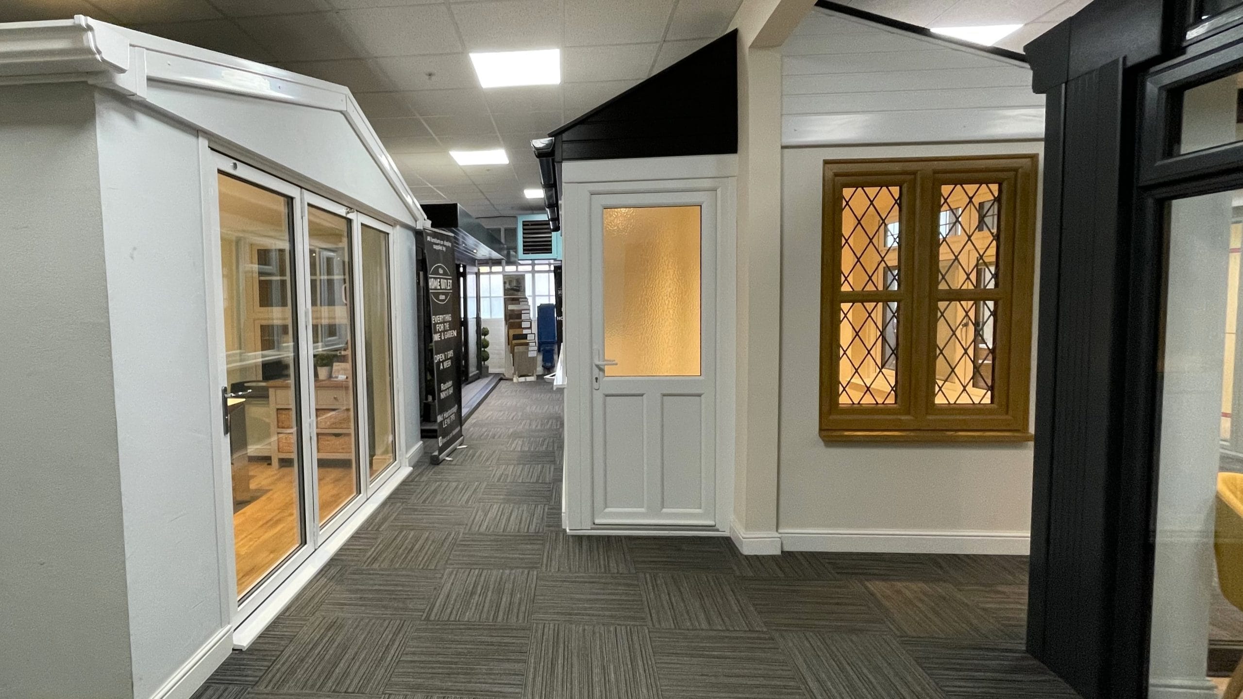 Inside Park Lane Windows showroom displaying white bi-fold doors, a white uPVC door, and a gold leaded casement window on display