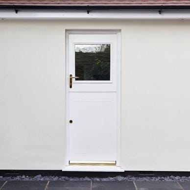 White composite stable door with glazed top panel and brass handle, set in a rendered exterior wall