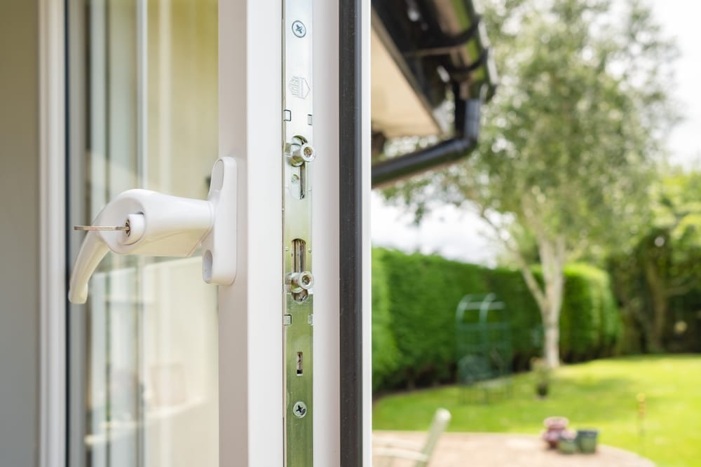 Close-up of a white uPVC door multi-point locking mechanism with handle, garden visible in background