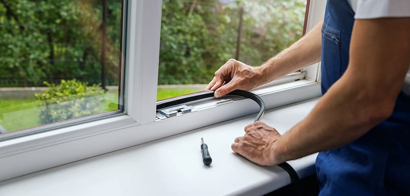 Installer fitting a new rubber seal into a white uPVC casement window