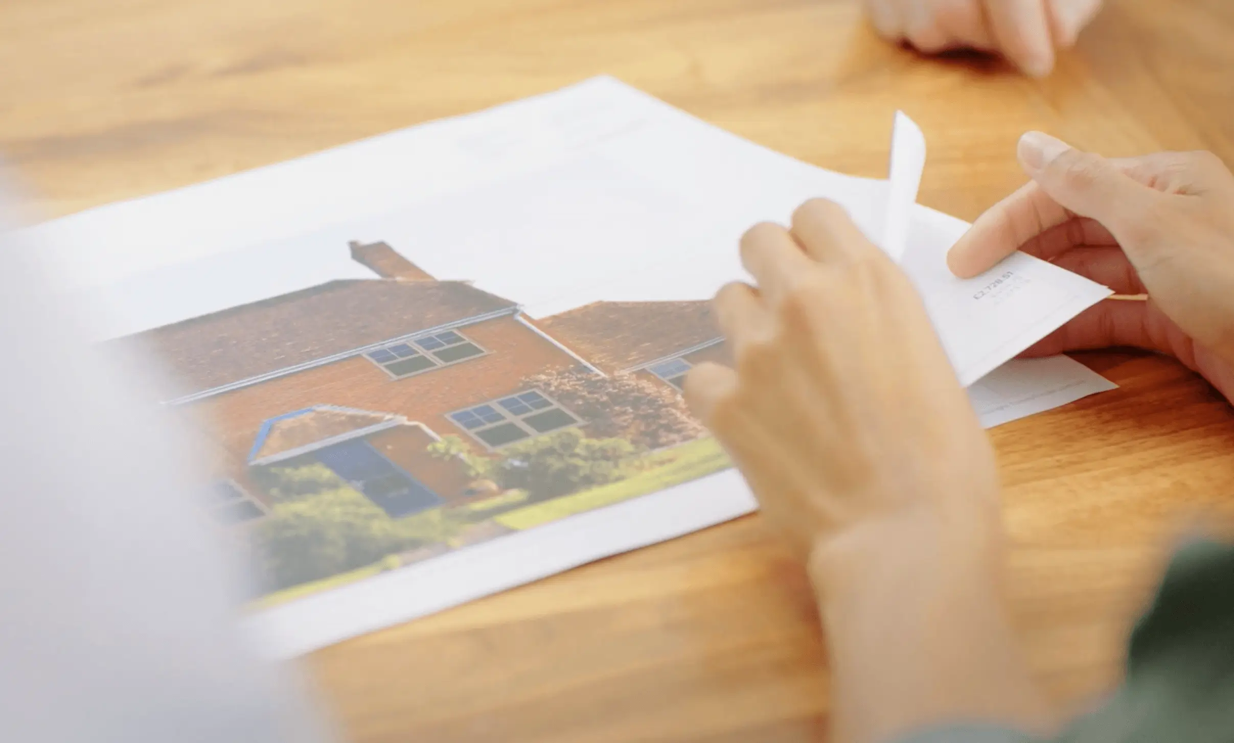 A customer reviewing printed house design plans showing windows and a front door on a brick home